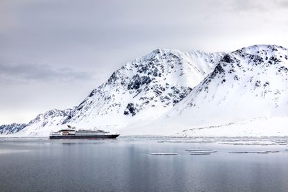 A cruise ship in the Arctic, with snow-covered cliffs in the background.