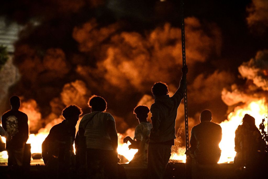 People look at burning tyres blocking a street in Bordeaux during civil unrest and protests following the killing by police of 17-year-old Nahel M in Nanterre on Tuesday