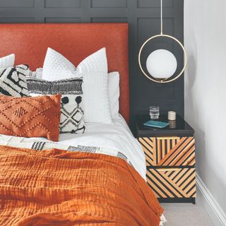 A bedroom with a panelled black feature wall, large orange headboard and lots of pillows and cushions on the bed