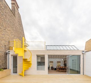 A back entertainment area with wooden decking, a yellow twirling staircase, a glass roof and a sliding door into the dining area.