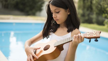 Young girl playing ukulele by the pool 