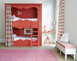 A red bunk bed with a red and white curtain and a pink floor rug