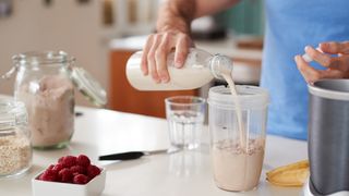 Close-up of person making a protein shake, pouring milk into blender jug