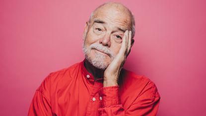 An older man has his hand on the side of his face and head tilted like he's embarrassed to be asking.