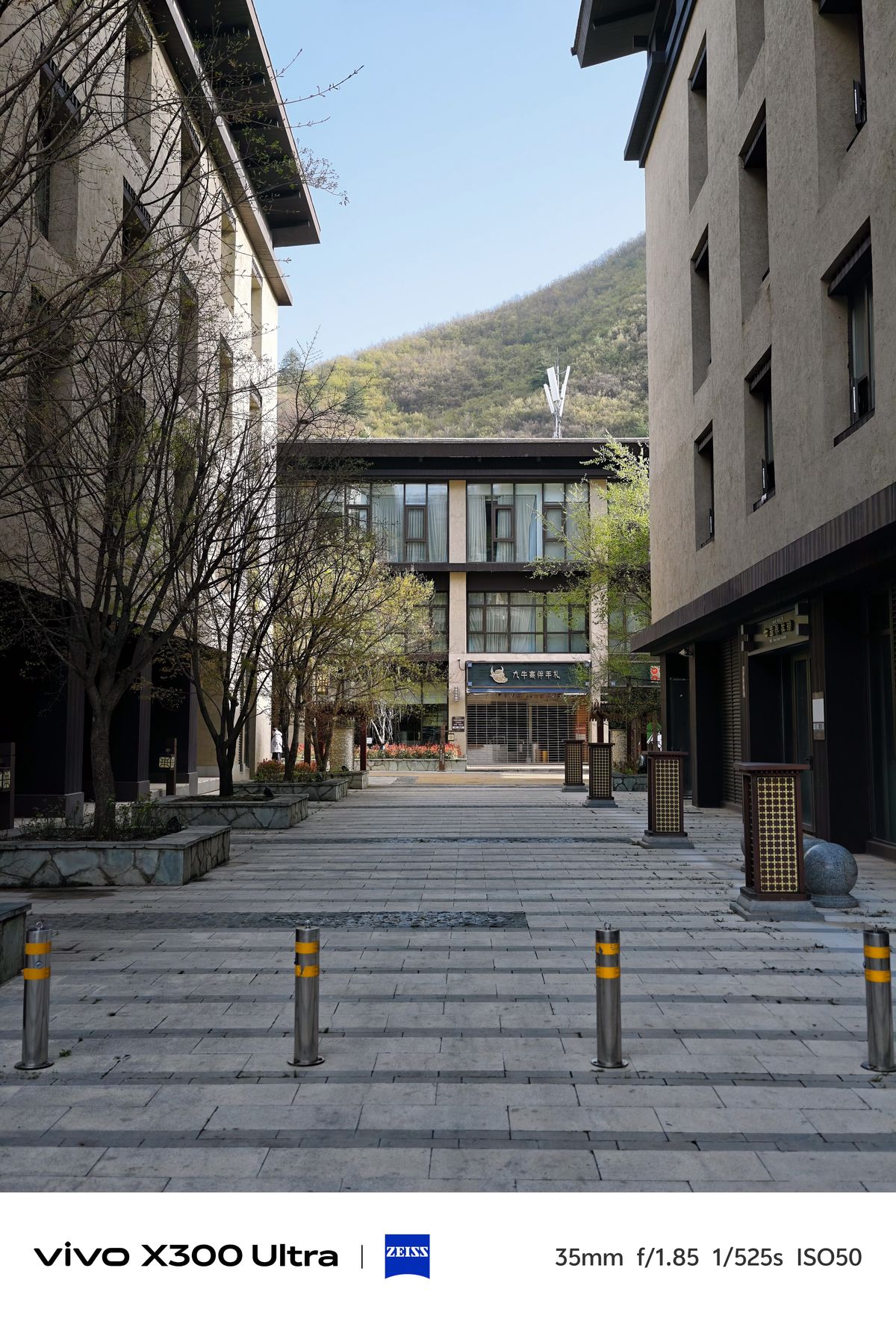 A paved pedestrian path stretching between contemporary buildings toward a green hillside.