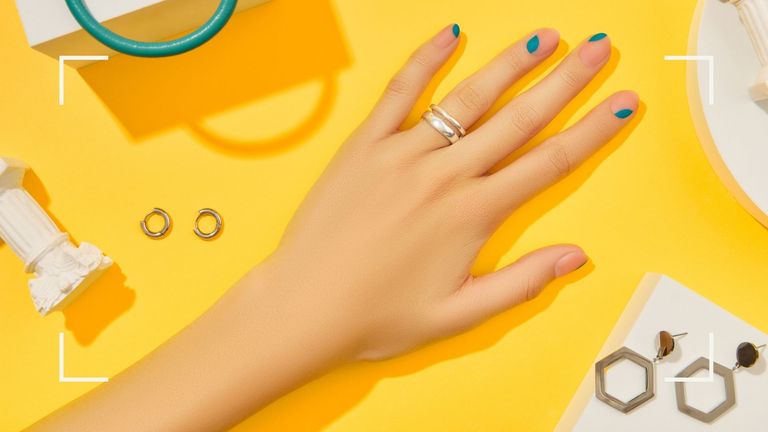 A woman's hand with blue irregular French tip nails on a yellow backdrop 