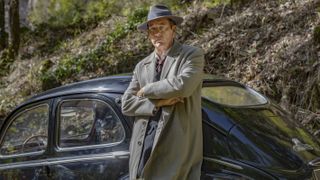 Sam Spade (Clive Owen) leans against a car in Monsieur Spade