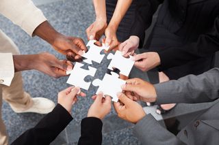 A group of people stand in a circle bringing four puzzle pieces together