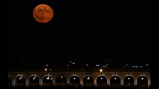 A plane flies in front of the Buck Moon supermoon over Pont de Bercy in Paris, France, on July 3, 2023.