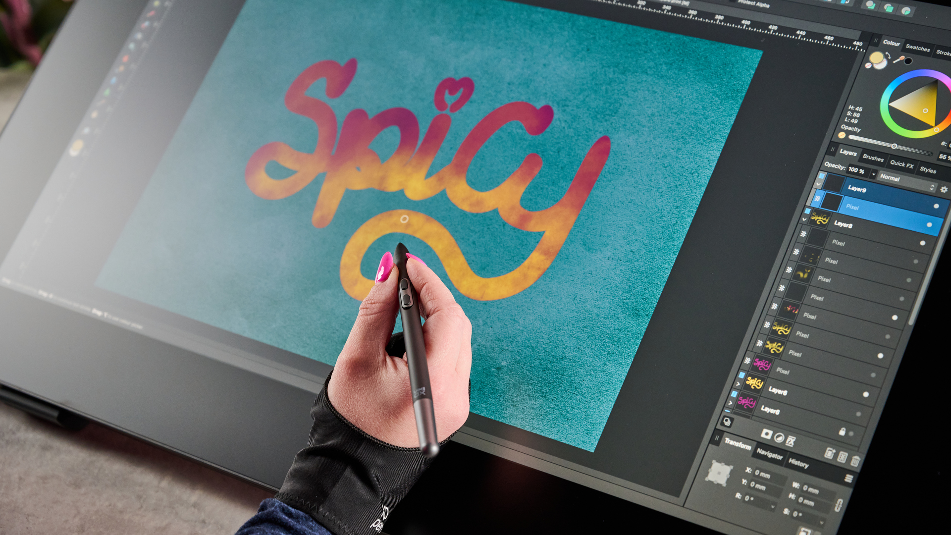 A woman's hand is holding a slim stylus over the drawing display, she is putting the finishing touches on some bright brush lettering that says"Spicy".