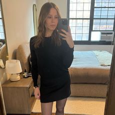 Nikki wears a black minidress, sheer brown tights, and black heels.