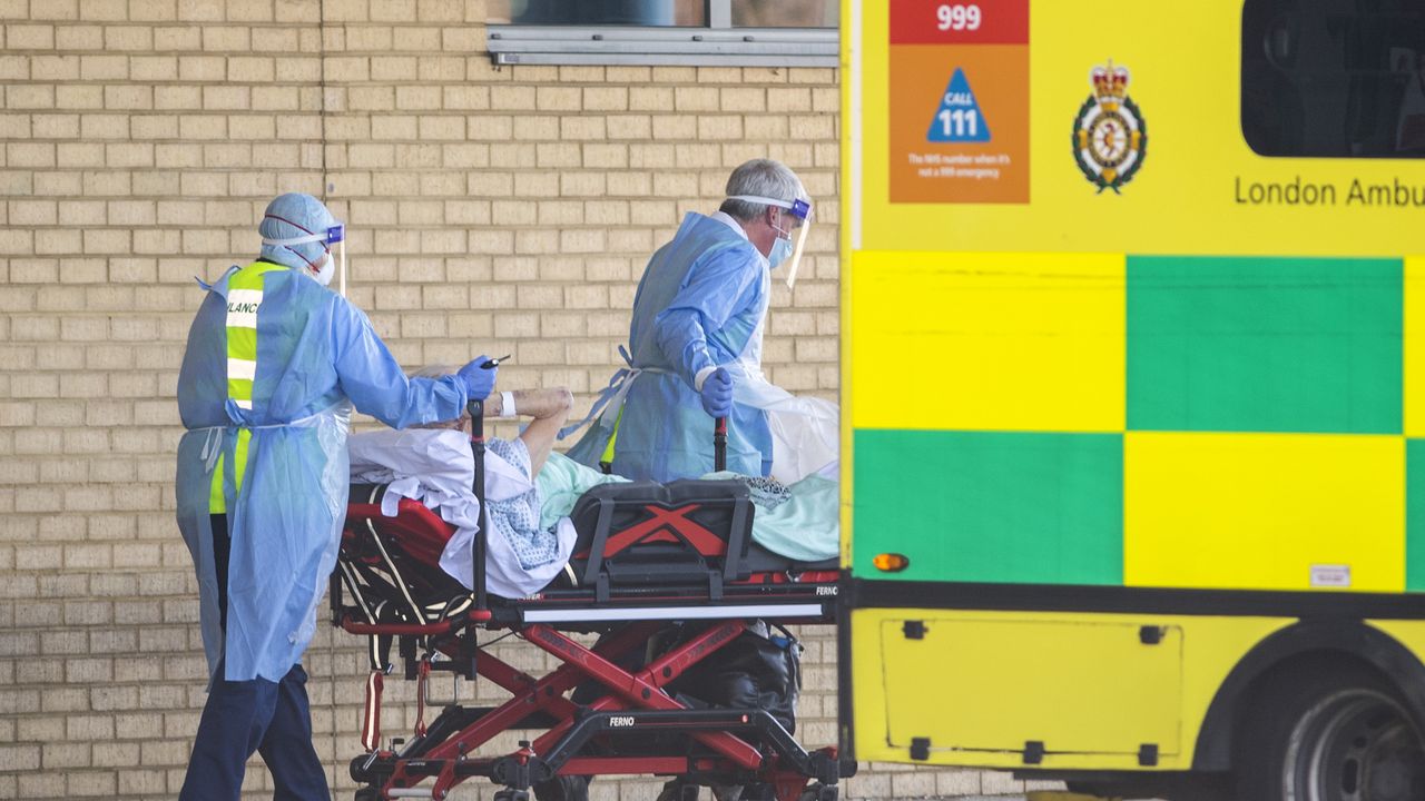 NHS workers in PPE take a patient into Queens Hospital, London