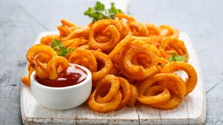 Curly French fries on white board with tomato sauce