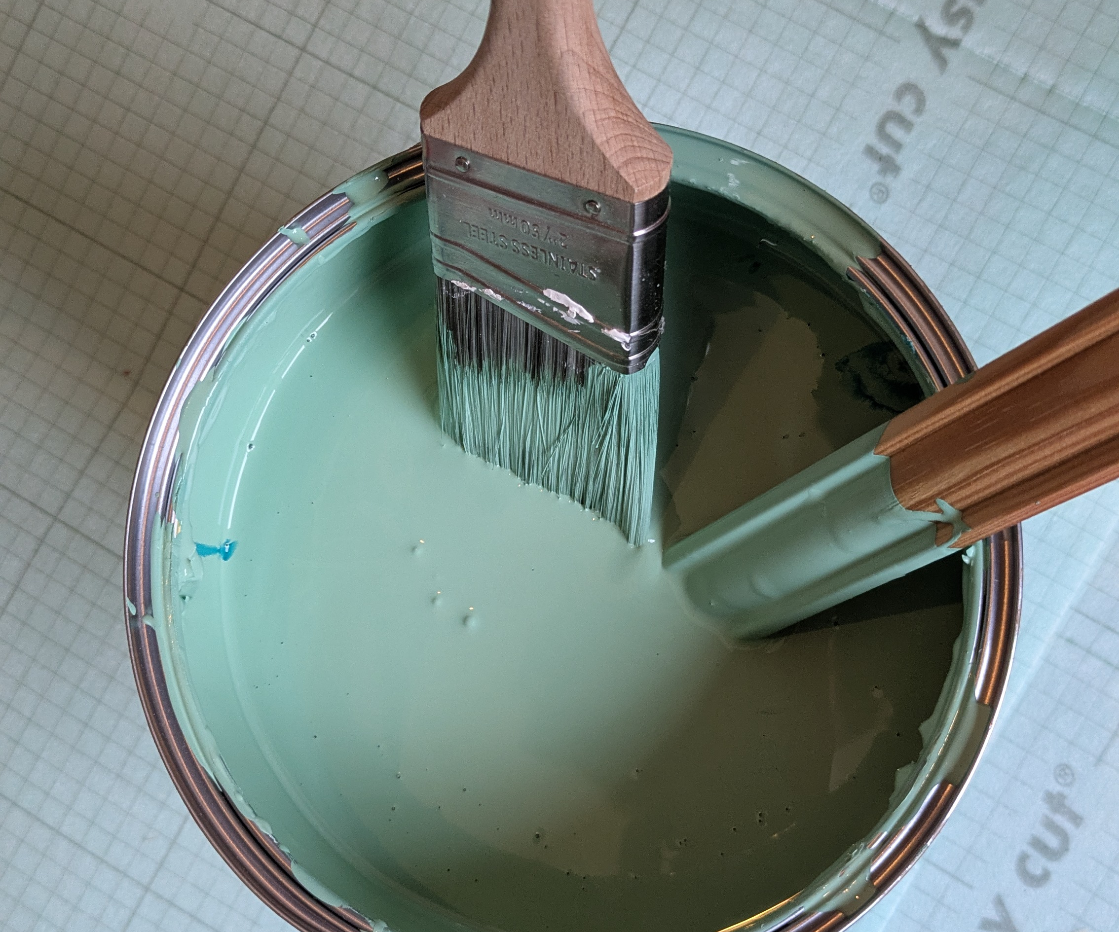 open tin of green paint with brush and wooden stick placed in paint