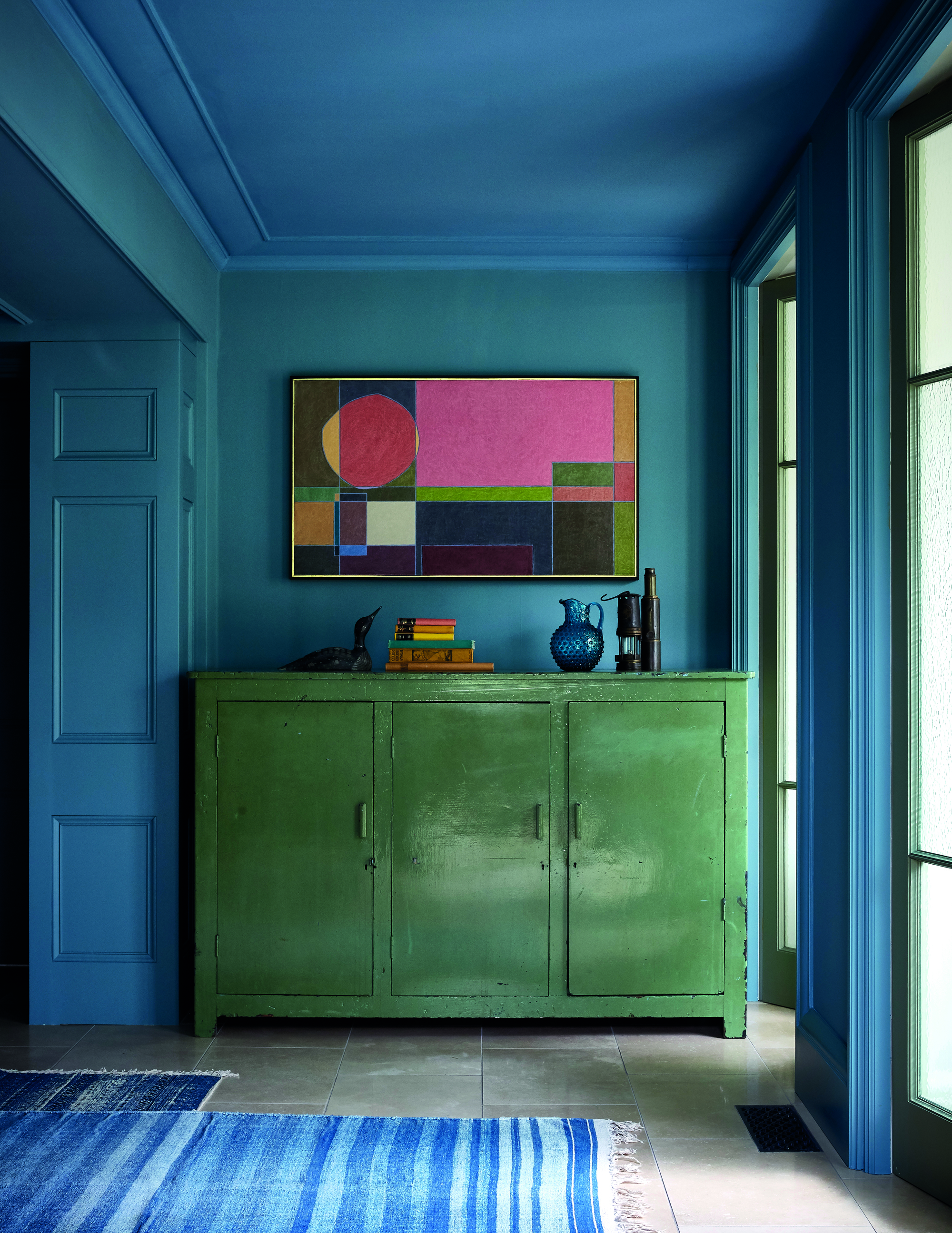 A green cabinet against a light blue wall in an entryway that is color drenched in a bold blue.
