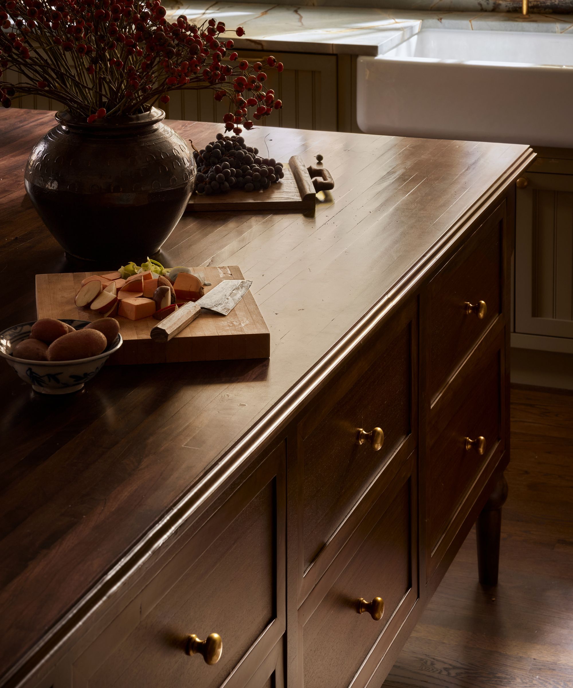 A close-up of a wooden freestanding kitchen island with deep drawers, brass hardware and turned legs