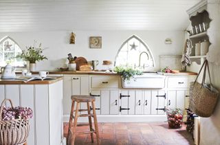 country kitchen with pale painted cabinets and gothic arched windows in cottage home with quarry tiles and wooden worksurfaces
