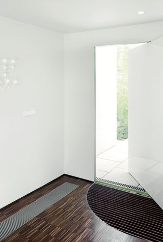Interior view of Gerry McGovern’s entrance hall featuring light coloured walls, a white wall mounted coat rack, wood flooring with a fitted door mat and a partially open white door offering a view of outside