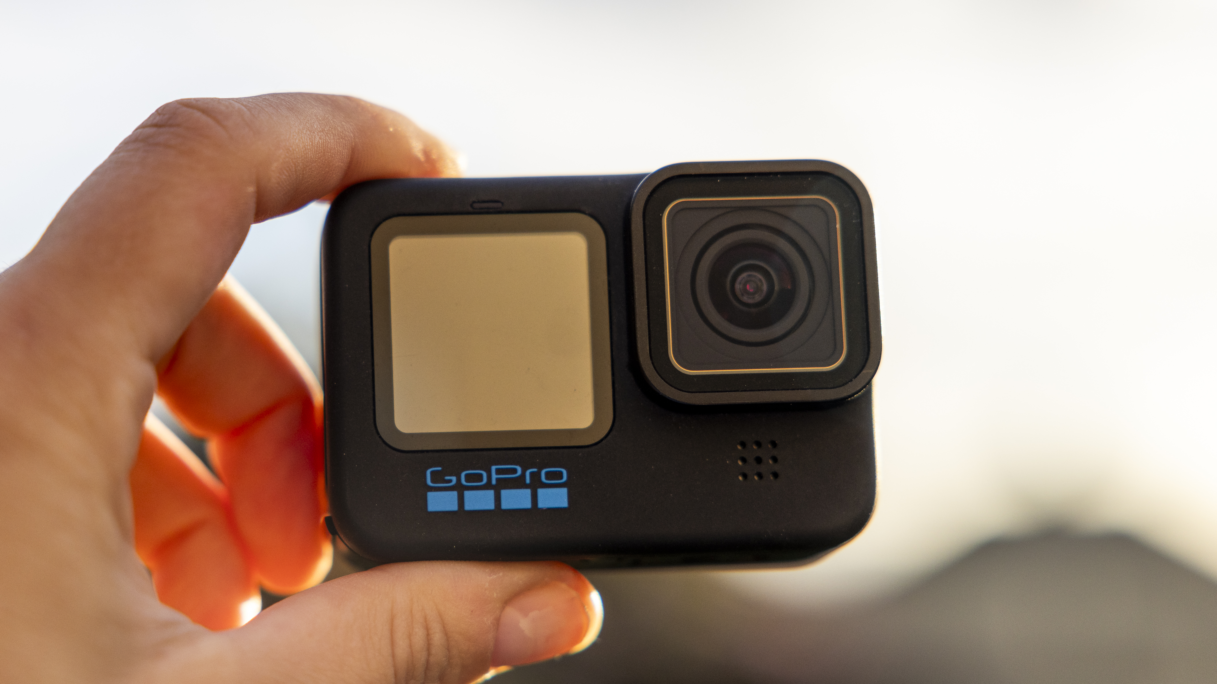 A GoPro Hero 12 Black being held with a backlit sun behind