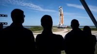 silhouettes of the back of four people looking at an orange rocket.
