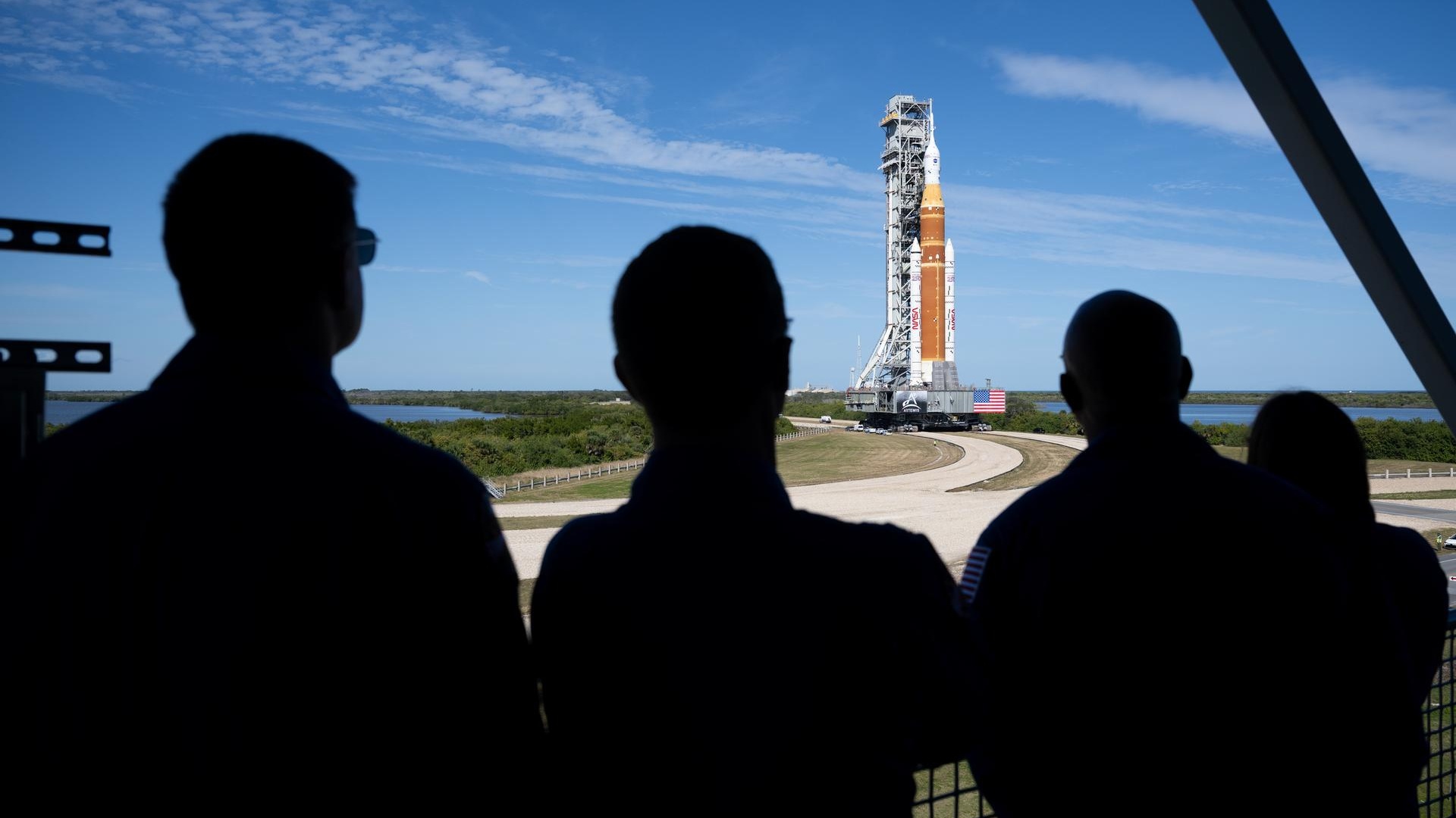 silhouettes of the back of four people looking at an orange rocket.