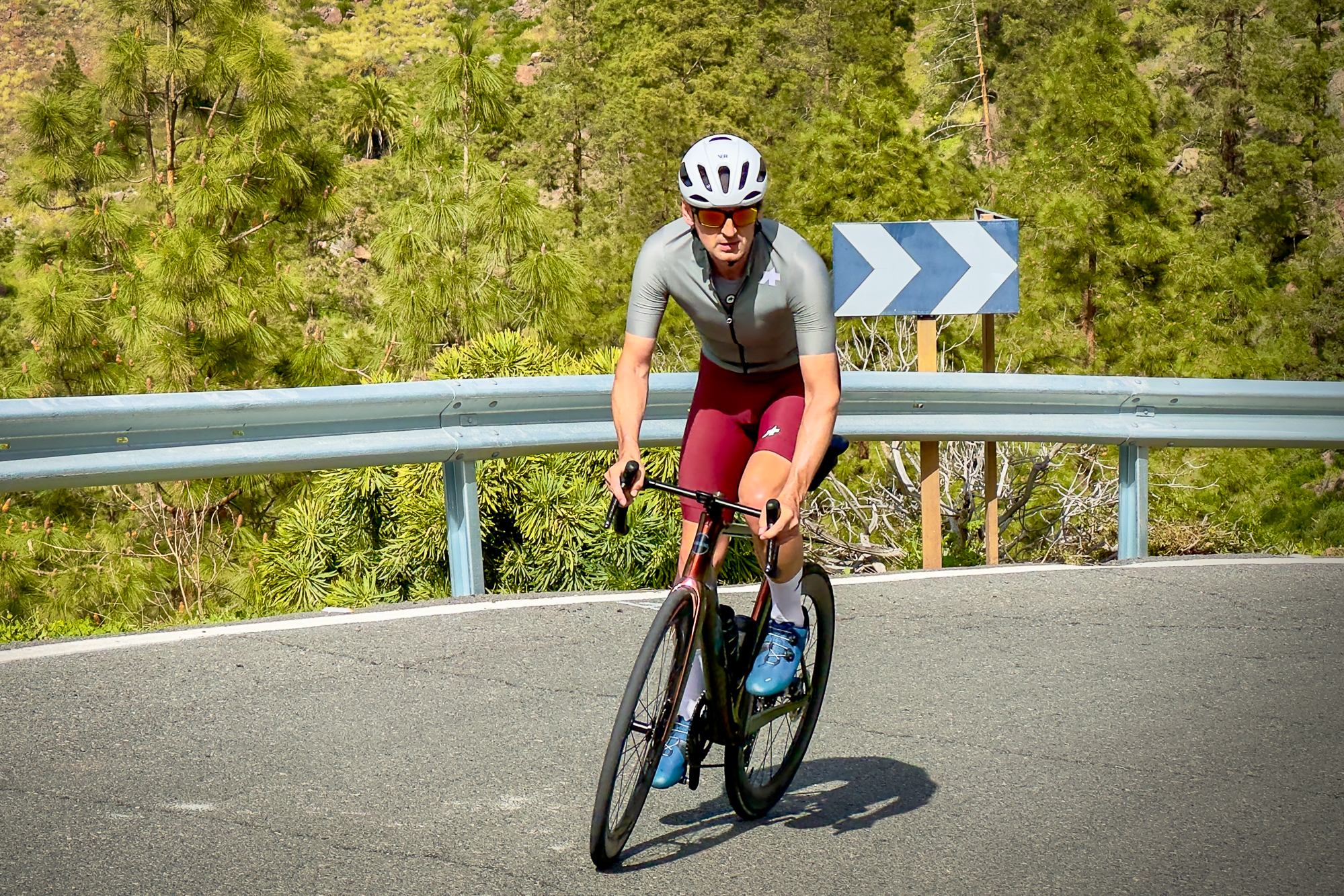 Man wearing a green jersey, red shorts and white helmet riding a road bike up a hill out of the saddle