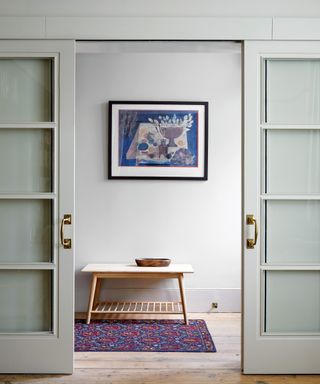 neutral hallway with sliding glazed doors, pale wood console table and blue and red rug