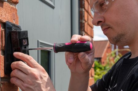 A man installs a video doorbell beside his front door.
