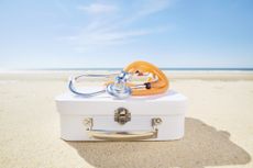 Stethoscope and suitcase on beach by the sea.