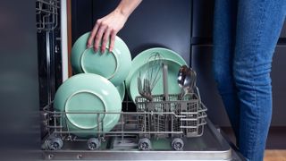Someone stooping to load green plates into a dishwasher