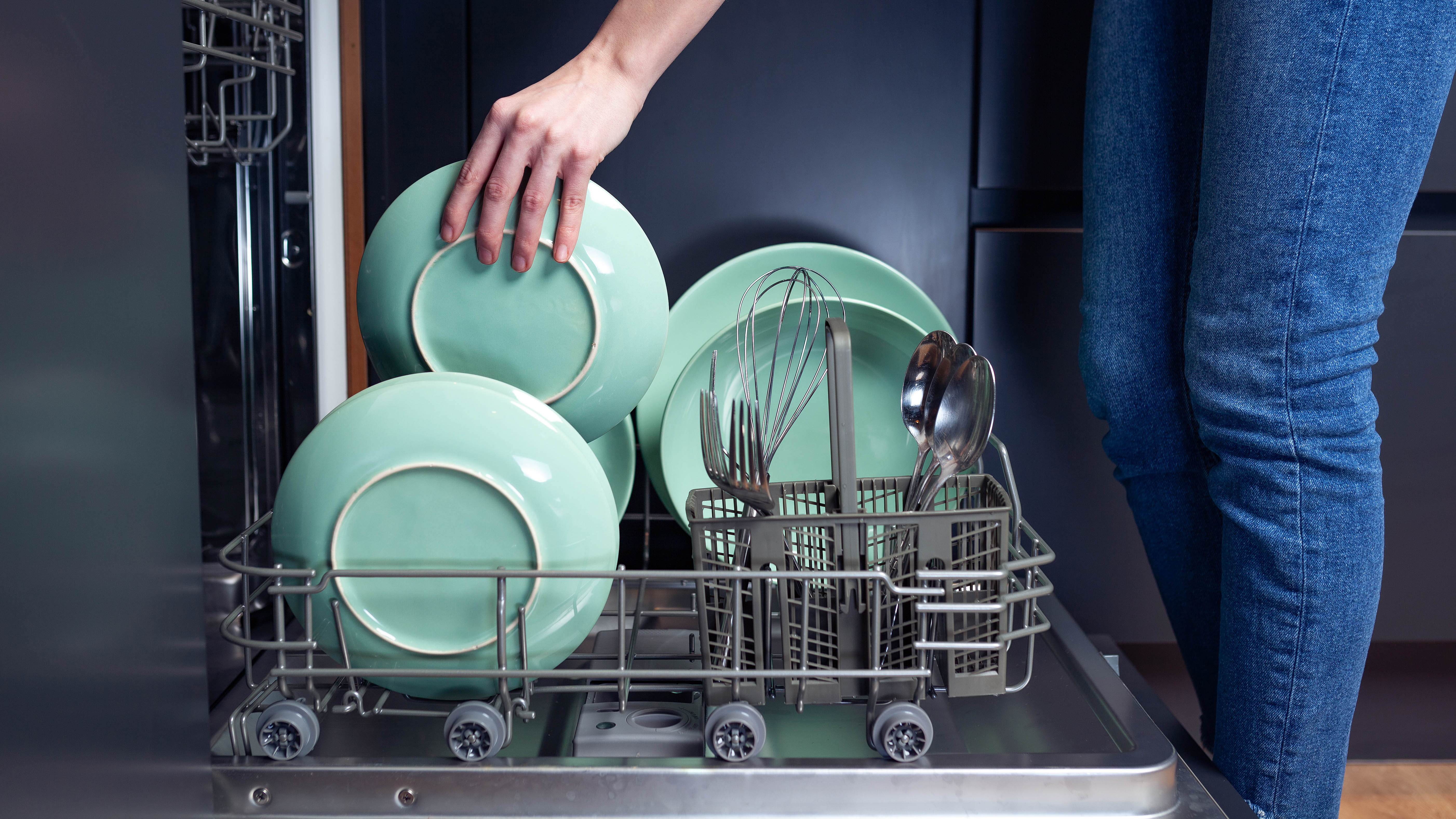 Кто-то наклонился, чтобы загрузить зеленые тарелки в посудомоечную машину.