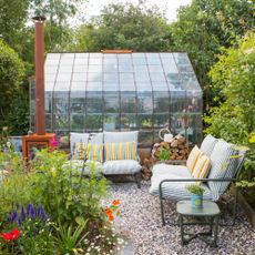 A gravel garden with two John Lewis Marcy 2-seater sofas in green stripe in front of a greenhouse