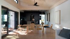 open plan living dining room with cork flooring, timber ceiling, timber dining table and chairs, and a dark black kitchen at the end of the room