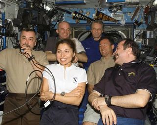 a group of five men and a woman smile while floating in a space station.