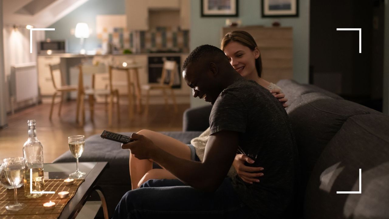 Romantic couple laughing together on the sofa in the living room, drinking wine from glasses, representing sex on the sofa