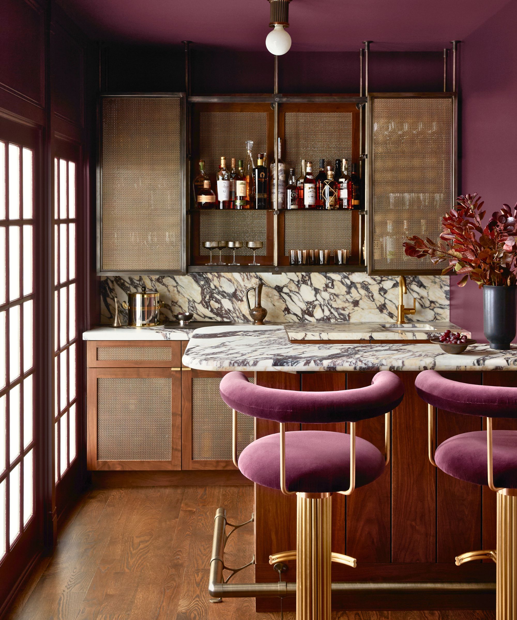 home bar with dark pink walls, wooden cabinets and marble counter
