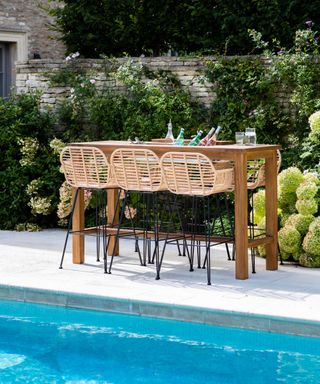 teak garden table with drinks cooler and wicker bar stools by swimming pool