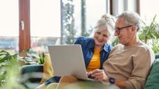 A couple sitting on the couch looking at their laptop