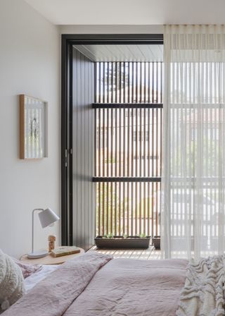 A sheer curtains hangs in a bedroom with an open door next to a balcony.