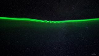 ripples of green waves in the northern lights which appear as a band of green ribbon across the star studded sky.
