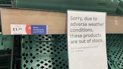 Empty green produce bins with two signs, one reading ‘Sorry, temporarily out of stock’, the other reads ‘Sorry, due to adverse weather conditions, these products are out of stock’.