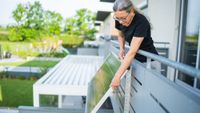 woman fitting solar panel to metal balcony