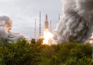 a rocket takes off above lush green vegetation in the foreground