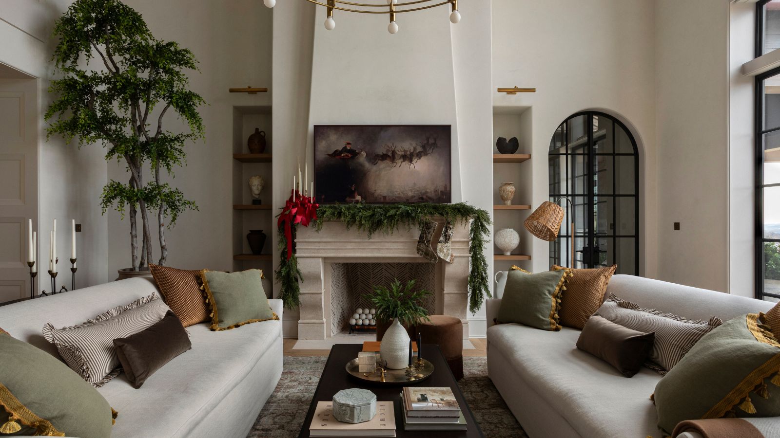 A white living room decorated for the holidays with a garland over the mantel, adorned with large red ribbons