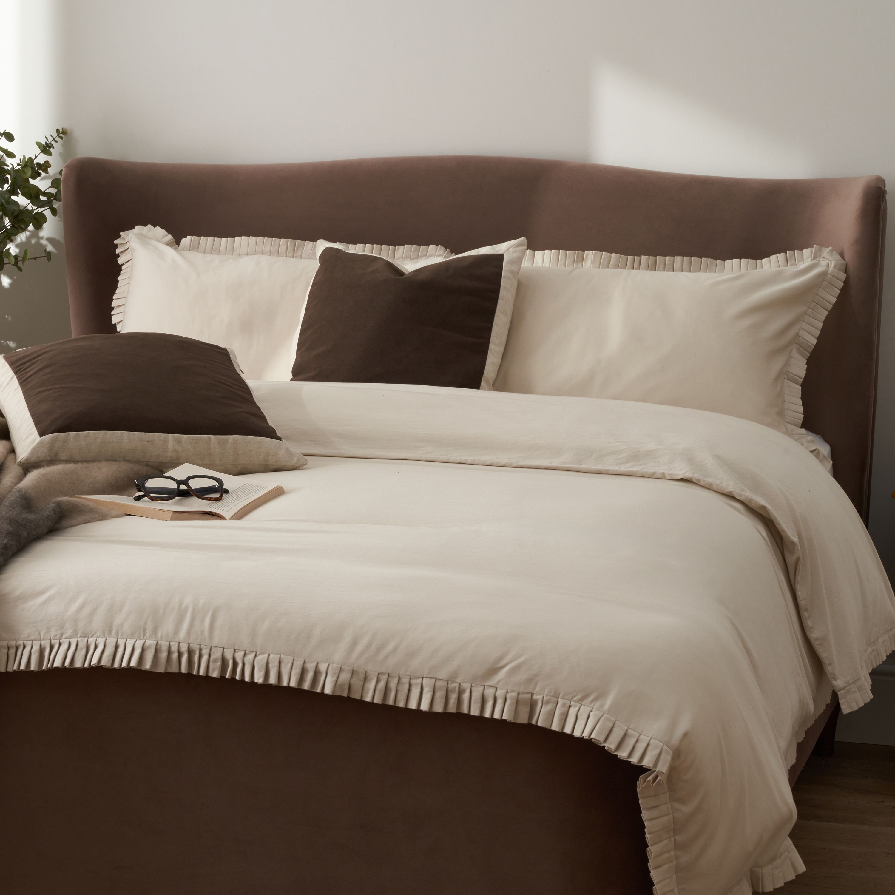 a brown bed with beige ruffled bedding