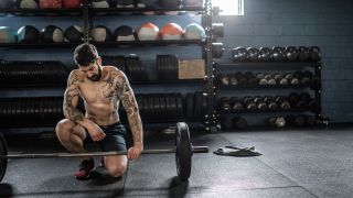 Man kneels next to barbell