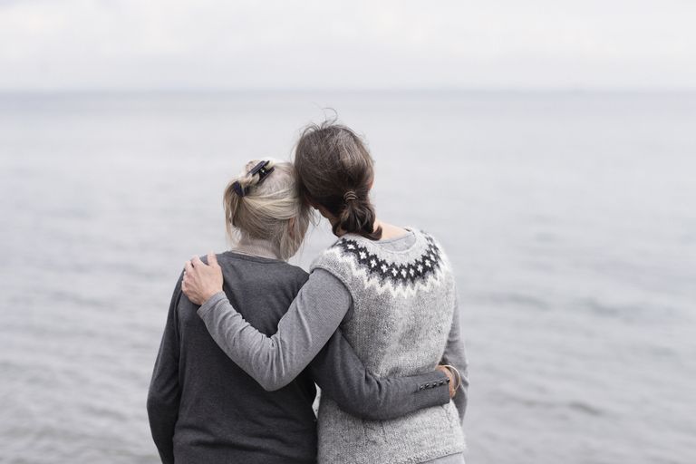 Two women of different ages hugging while looking out over a grey sea.