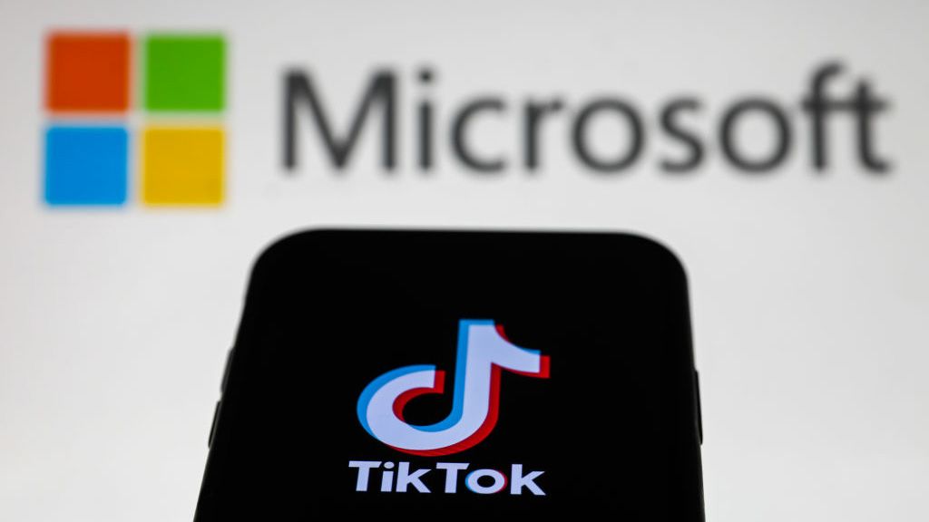 Phone with TikTok logo on screen in front of white background with blurry Microsoft logo 