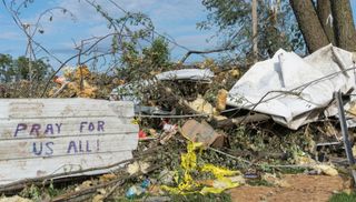 Uma foto de escombros e destroços de um tornado, com uma placa pintada dizendo 