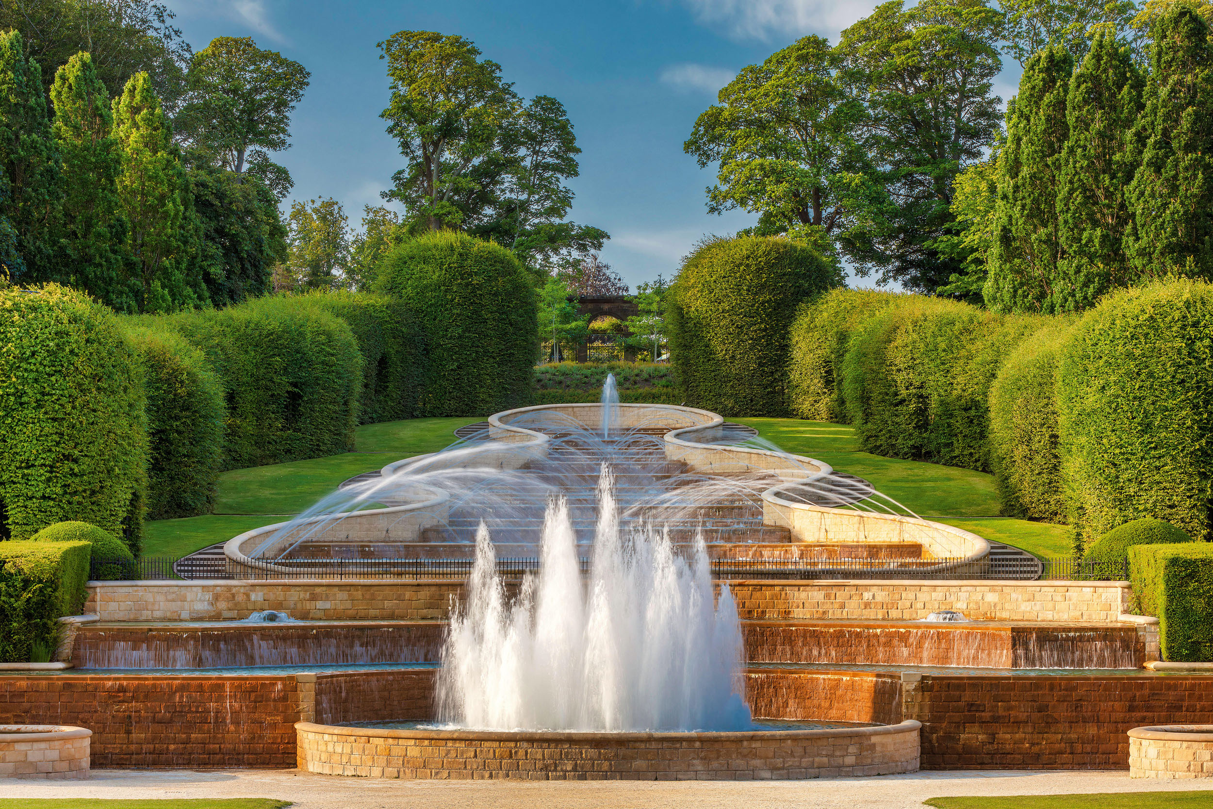 A view on a sunny summer evening of the Grand Cascade in the Alnwick Garden in Northumberland looking towards the Walled Garden.